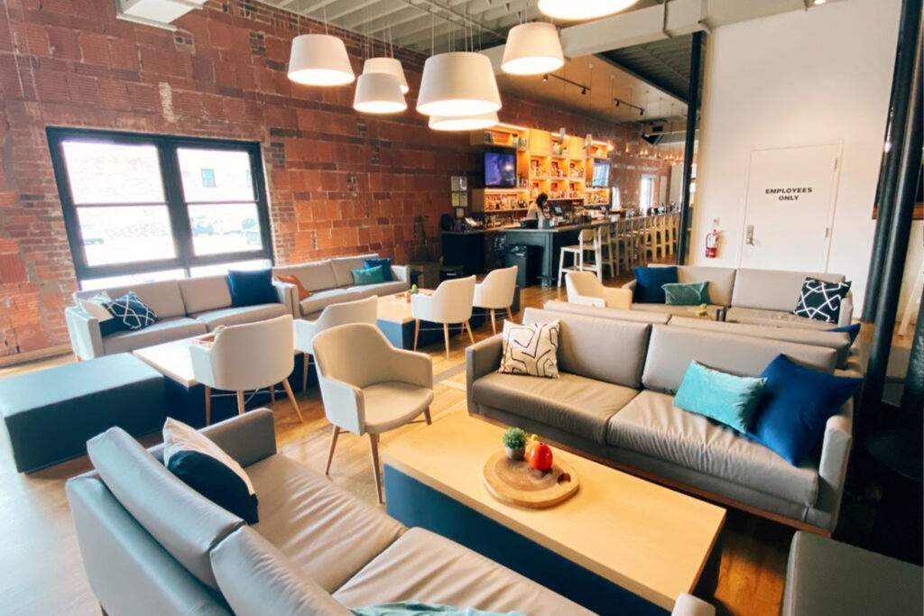 Patio room decorated with soft grey couches. Large hanging white lamps shades make a lighting feature. A full service bar lines the back wall.